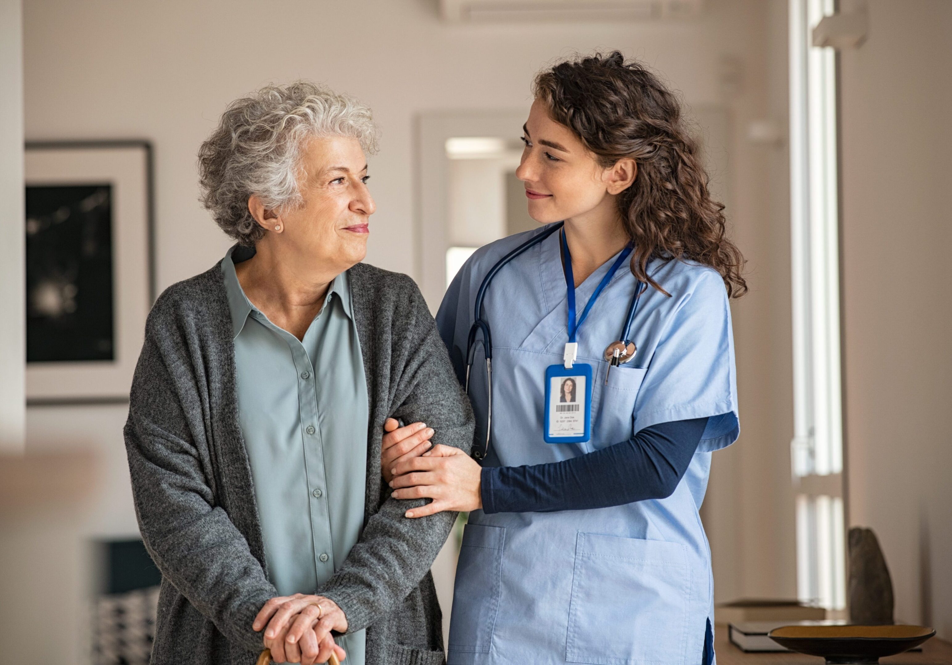 Young caregiver helping senior woman walking. Nurse assisting her old woman patient at nursing home. Senior woman with walking stick being helped by nurse at home.