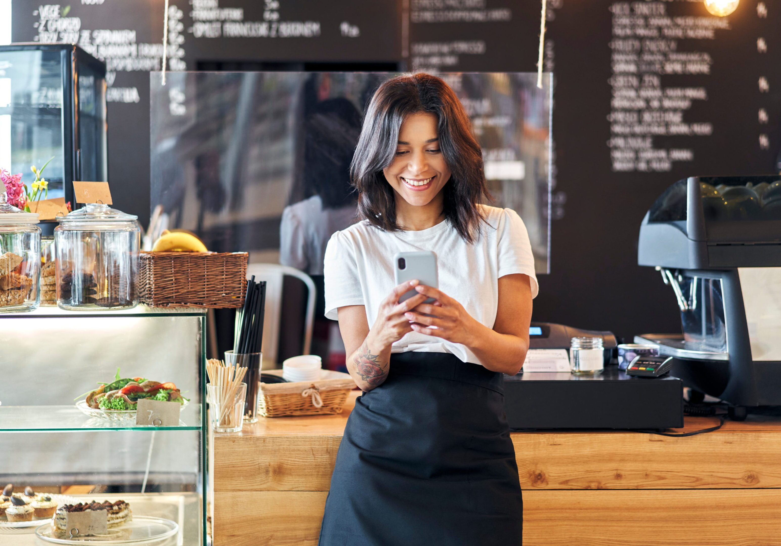 Portrait of smiling waitress barista using mobile phone at work