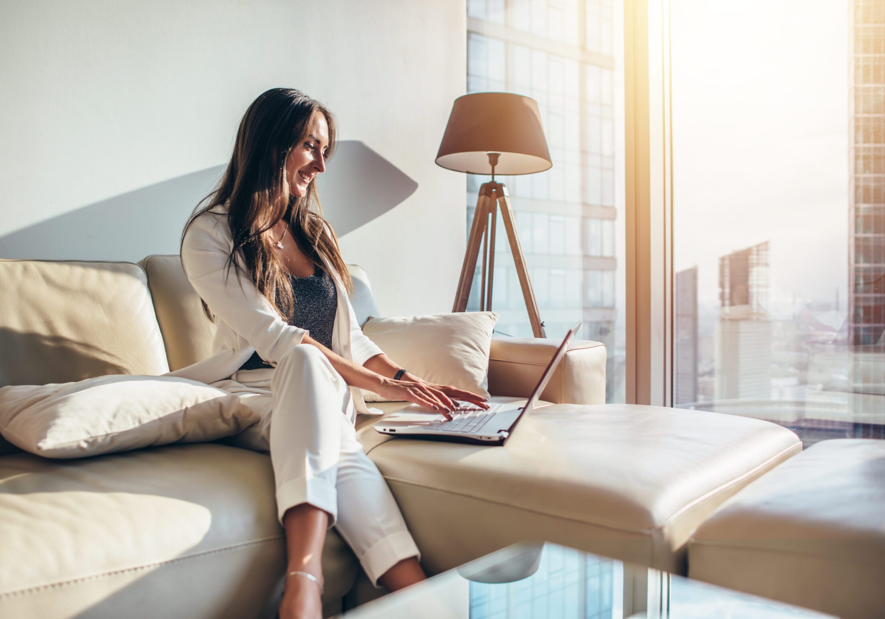 Elegant young female business woman using a laptop sitting on a sofa at home.